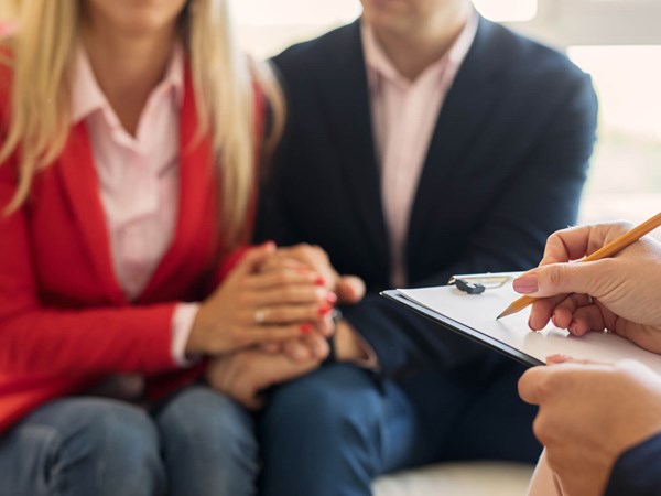 Concerned Couple Couple sat holding hands and woman with clipboard